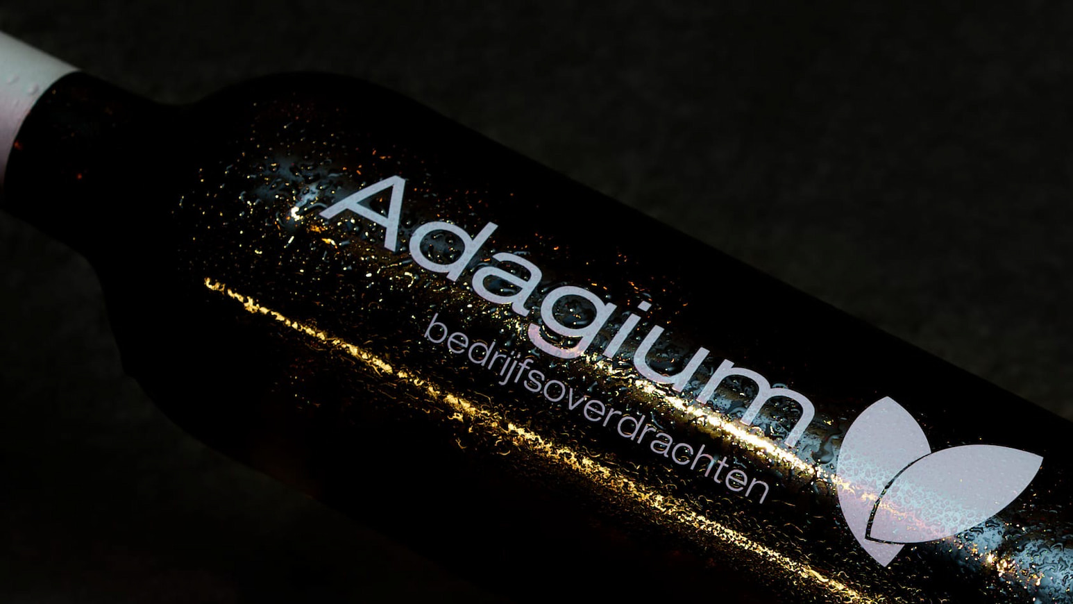 Donkere fles met het logo en de naam Adagium bedrijfsoverdrachten in witte letters en een lichtroze bladlogo.