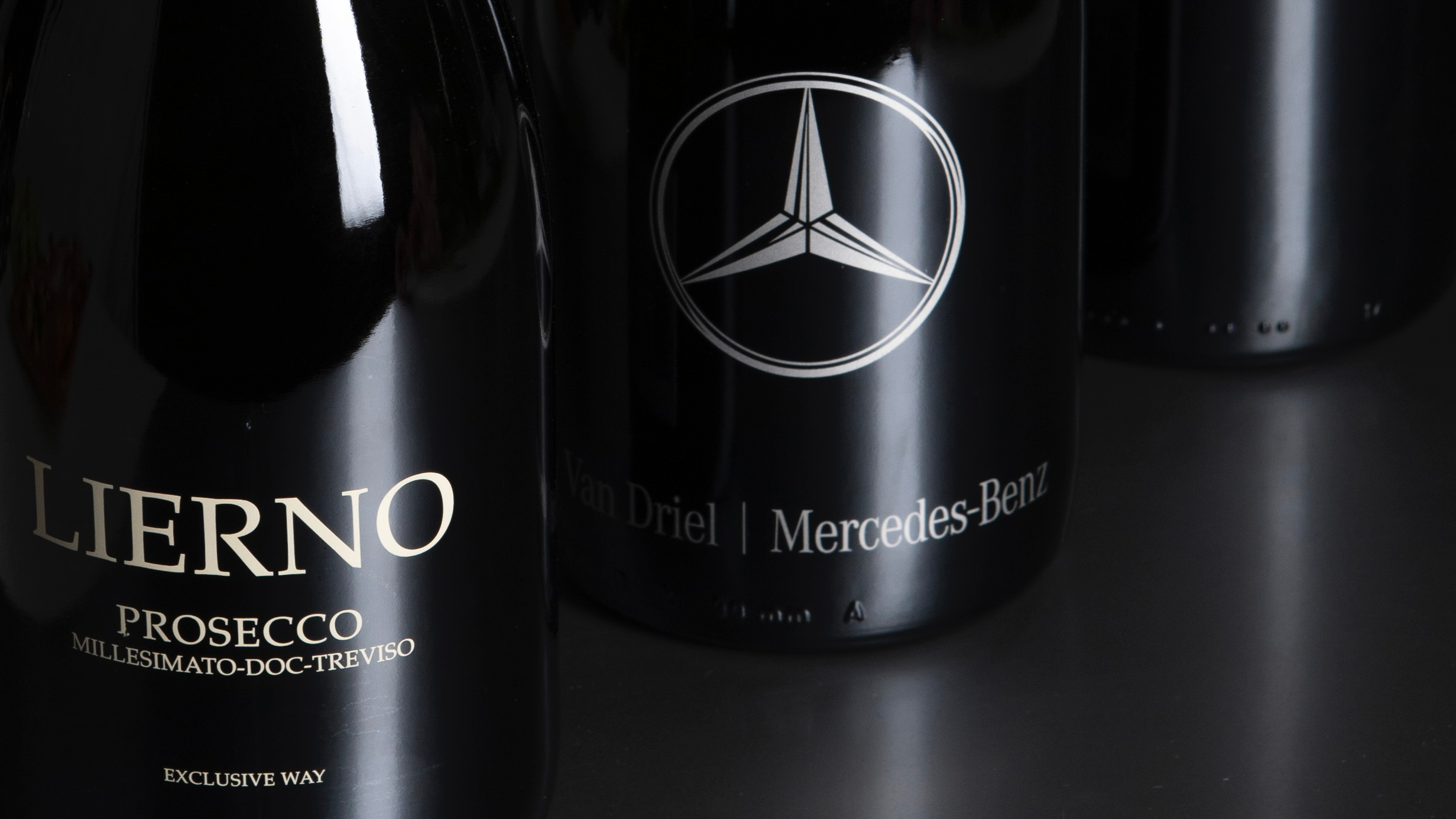 Zwarte flessen Lierno Prosecco met Mercedes-Benz branding op een donkere ondergrond.