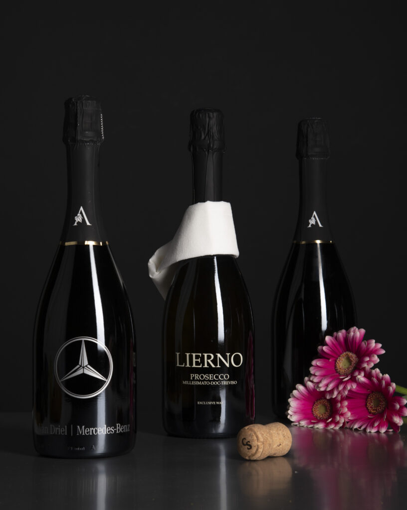 Drie flessen Lierno Prosecco met een kurk en roze bloemen op een donkere achtergrond.