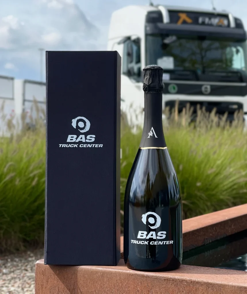 Fles en geschenkverpakking met BAS Truck Center-logo voor een vrachtwagen op de achtergrond.