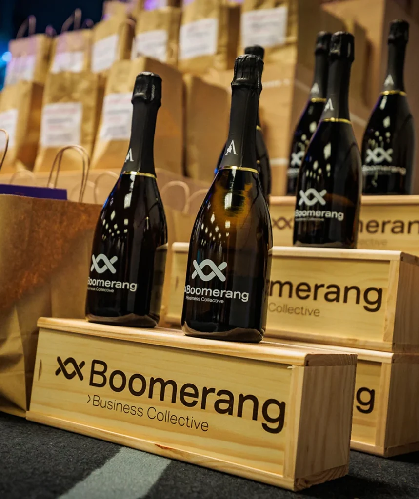Flessen Boomerang Business Collective champagne op houten presentatiekisten, omringd door papieren goodiebags.