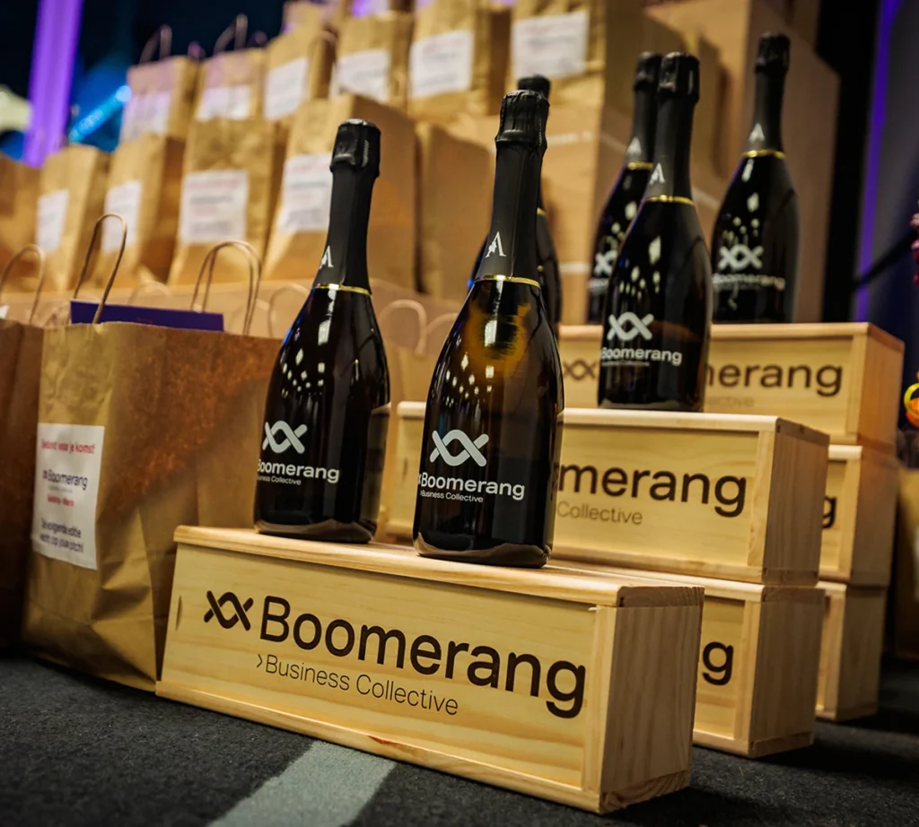 Flessen wijn met Boomerang-logo in houten kisten, omringd door papieren cadeauzakken.